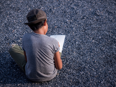 The boy is sitting drawing on a gravel floor.