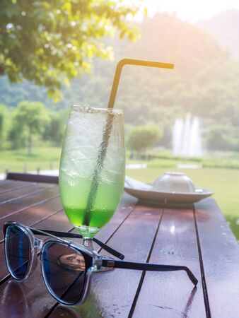 Green cocktail and sunglasses resting on a wooden table with a natural background.の写真素材