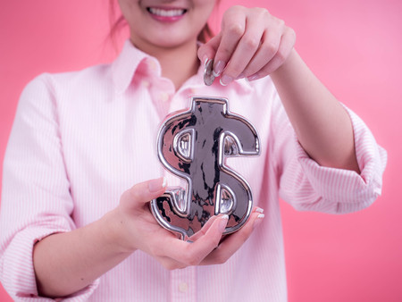 Woman hand putting a coin into financial symbol bank. Concept of future, business, saving money, economy and investmentの写真素材