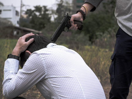 Portrait of Killer hand holding gun and put gun to businessman head.
