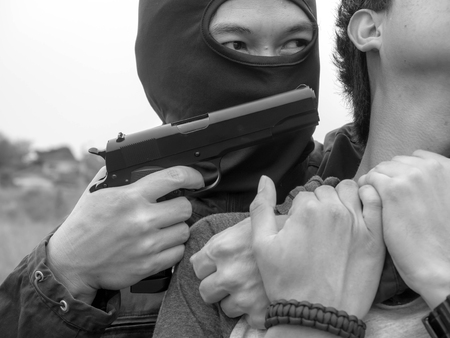 The robber holds the gun to take the man hostage of terrorist, Criminal and robbery for man safety concept. White and blackの写真素材
