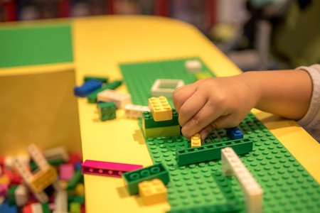 Close up of child's hands playing with colorful plastic bricks at the table. Early learning. stripe background. Developing toysの写真素材