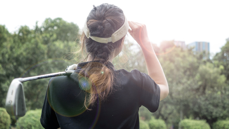 Close up back of a pretty woman on the green just finishing her swing. She is looking  to the draw of her ball that hit out to the sight.の写真素材