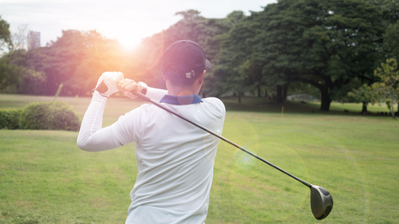 Golf player hitting beautiful shot with club on course with sun flare in backgroundの写真素材