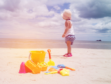 Little girl standing with toys on tropical sand beachの写真素材