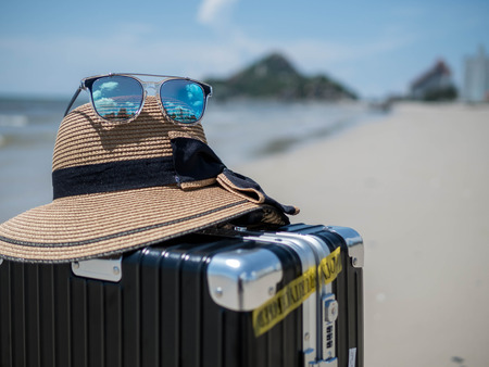 Travel suitcase, hats and sunglasses on a beach ocean in the background. Tropical sea, Summer holiday traveling concept design banner with copyspace.の写真素材