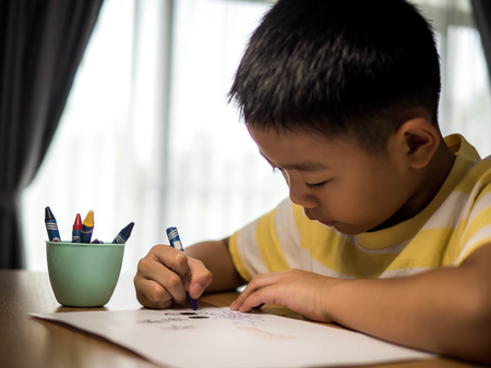 Boy sitting at the chair at table draws on the paper in bedroom.のeditorial素材