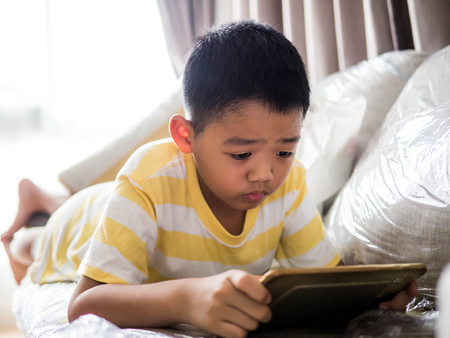 Young boy lying on a sofa and playing games in a mobile phone.
