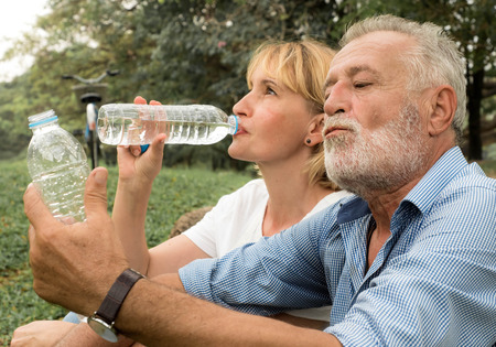 Senior couple sitting together at park on summer health care drinking water, Happy lifeの写真素材