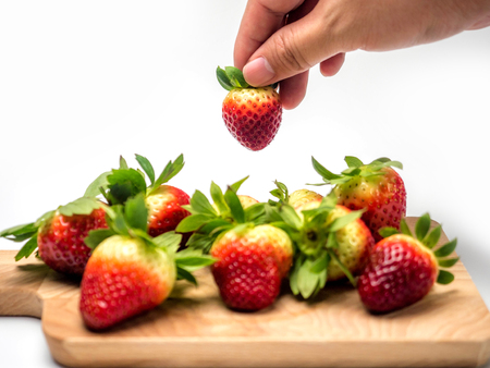 Hand picking strawberry from heap of fresh strawberries on wooden tray for diet, isolated on white background.の写真素材
