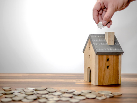 Household savings and finances, Hand putting coin in house model bank. Saving money conceptの写真素材