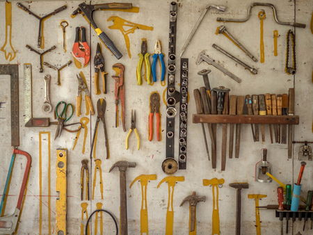 Many different rusty old tools hanging on a wall in workshop