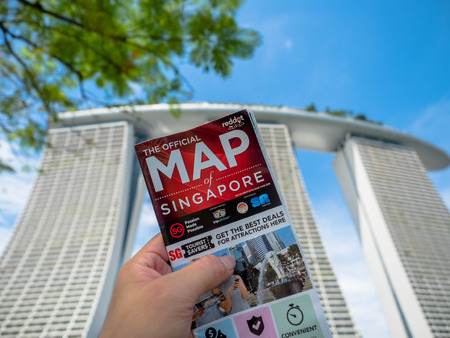 Singapore - Nov 24, 2018: Man holds a map of Singapore and background is Marina Bay Sands Hotel.