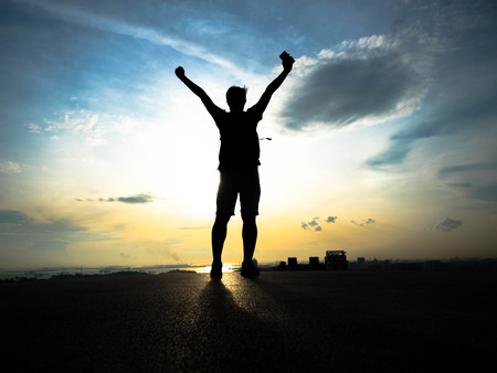 Silhouette man rising hands standing on the top viwe on the picturesque sunrise background Overlook...