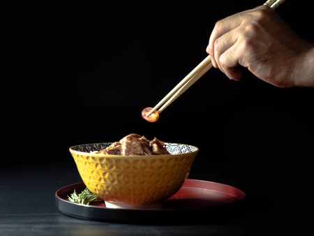 Hand use bamboo stick for Rice topped with pork isolated on black background, raw food Japanese food court concept.の写真素材