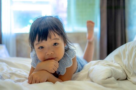 cute smiling little asian girl woke up in white bed.