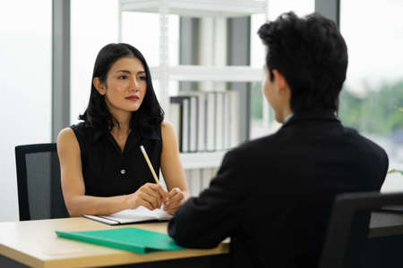 Beautiful manager woman talking to a male job applicant at the desk, interviewing, Rear view at a man. Business concept photoの写真素材