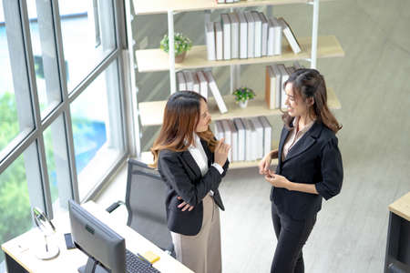 Young business woman talking with partner while standing in modern office interior, team of professional employees discussing ideas of project after meeting.の写真素材