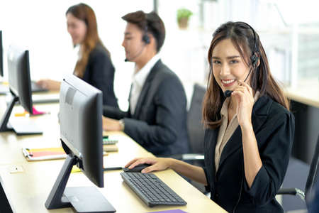 Call center worker accompanied by her team. Smiling customer support operator at work. Professional operator concept.の写真素材