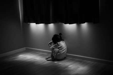 Squat single child sit near window, sad lonely in dark night indoor, crying, bad mood, offended, consoles,  concept of unhappy childhood, life togetherの写真素材