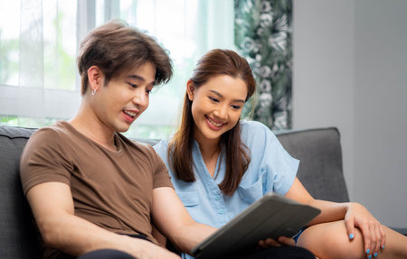 Young couple watching online content in a smart phone sitting on a sofa at home in the living room.の写真素材