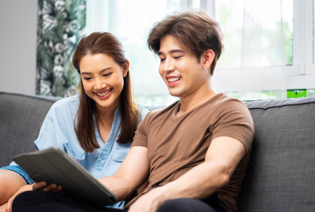 Young couple watching online content in a smart phone sitting on a sofa at home in the living room. Loving couple shopping online in internet store.の写真素材
