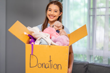 Happy volunteer woman holding box with donated toys indoors. Donation Concept.の写真素材