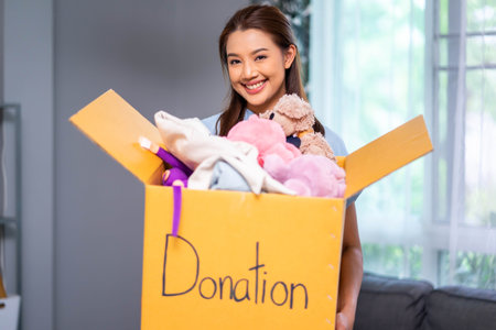Happy volunteer woman holding box with donated toys indoorsの写真素材
