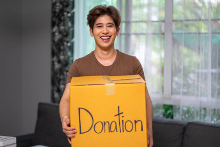Happy volunteer man holding box with donated toys indoorsの写真素材