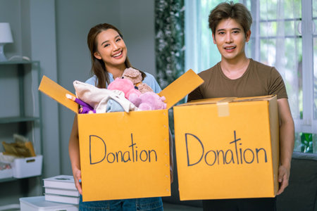 Portrait of happy Young couple packing stuff clothes donation boxes to another peopleの写真素材