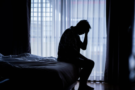 Lonely man silhouette sitting on the bed feeling depressed and stressed in the dark bedroom, Depression and anxiety disorder conceptの写真素材
