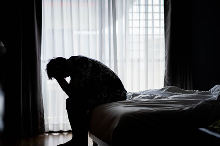 Lonely man silhouette feeling depressed and stressed sitting head in hands in the dark bedroom, Depression and anxiety disorder conceptの写真素材