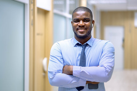 Young African businessman smiling while standing in a modern office, smiling at cameraの写真素材