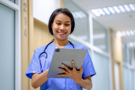 Closeup portrait of woman health worker wearing blue uniform In Hospital Corridor Using Digital Tablet.の写真素材