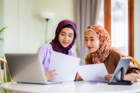 Two muslim women at home during lesson, studying near computer, online education. Culture, traditions, modern people.  shopping or talking.の写真素材