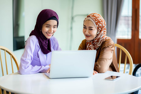 Two muslim women at home during lesson, studying near computer, online education. Culture, traditions, modern people.  shopping or talking.の写真素材