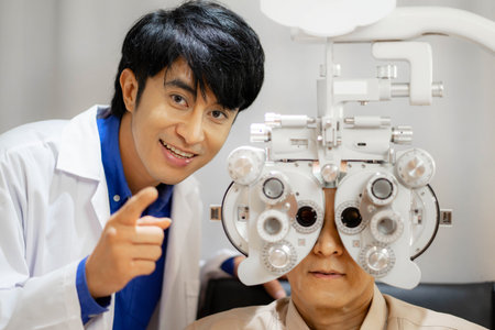 Male optometrist with phoropter while examining patientの写真素材