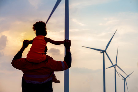 African child on father's shoulder against windmill background of evening sunset father and daughter conceptの写真素材
