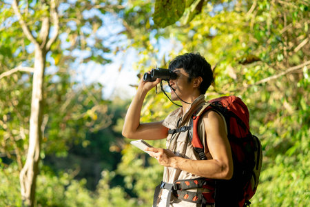 Asian young man with binoculars hiking in forest. Summer vacation.の写真素材