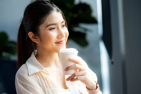 Relaxed woman looking away drinking coffee at home looking out the window enjoying the new day.の写真素材