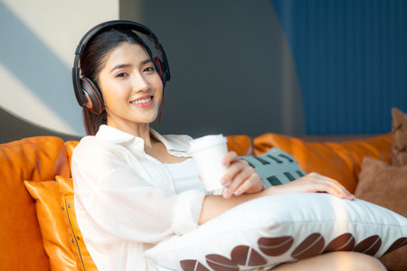 Portrait of a young asian woman using mobile phone and earphones to listening to music or online chatting at homeの写真素材