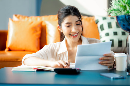 Happy woman paying bills accounting costs charges taxes and credit card expenses using calculator looking pleased and happy in e-banking and home finance concept.の写真素材