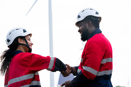 FeMale electric engineer and maintenance worker shaking hands in wind turbine farm. Agreement. Renewable energy.の写真素材