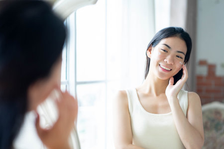 Young asian woman applying moisturizer on her face. Daily self-care routine.の写真素材