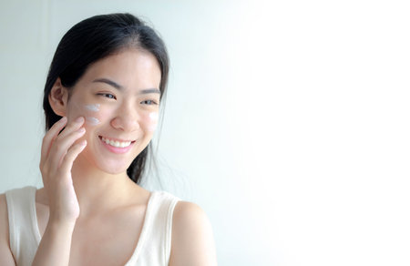 Happy young woman apply facial cream look in mirror, Skincare Cosmetic Products Concept.の写真素材