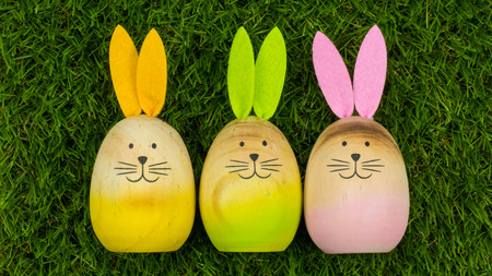 3 wooden bunnies with colorful ears lying next to eachother on green grass