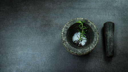 Mortar and pestle filled with sea salt, pepper and rosemary on dark stone background with free text spaceの写真素材