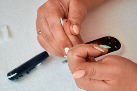 A diabetic checks his blood sugar. The woman is self-tested with a Lancet and a glucometer at home. Puncture of a fingerの写真素材