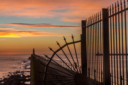 Tynemouth Pier and the Lighthouse through the metal railings with a beautiful vibrant sunriseの写真素材