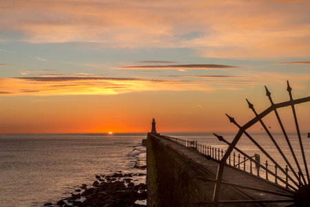 Tynemouth Pier and the Lighthouse through the metal railings with a beautiful vibrant sunriseの写真素材